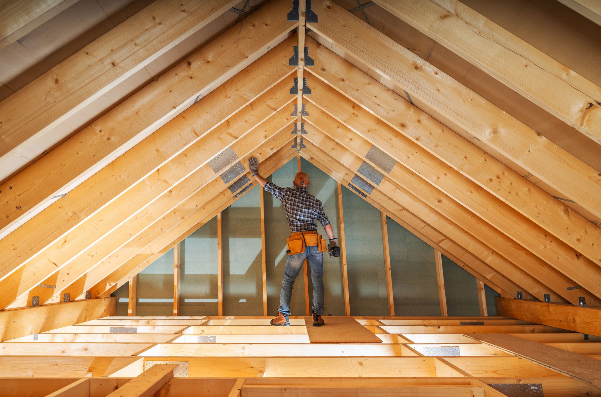 Worker Measures Roof Trusses in a Newly Built Attic During Construction on a Bright Day